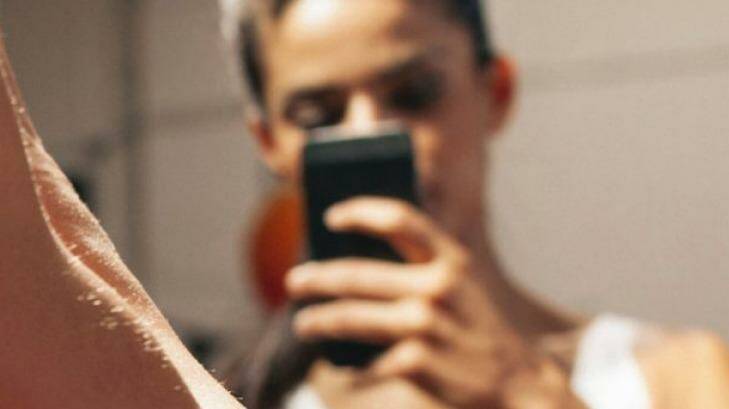 Sporty young woman taking a picture of herself in a mirror. Fitness model taking a selfie in front of a mirror in gym. Photo: iStock